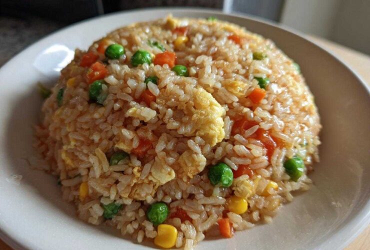 A close-up of a mound of homemade Vegetable Fried Rice with peas, carrots, corn, and scrambled egg on a white plate.