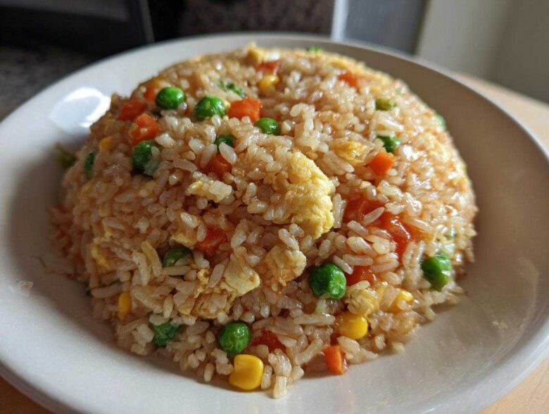 A close-up of a mound of homemade Vegetable Fried Rice with peas, carrots, corn, and scrambled egg on a white plate.