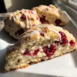 A close-up view of a freshly baked White Chocolate Raspberry Scone, showing its fluffy interior packed with raspberries and topped with white chocolate glaze.