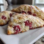 Three freshly baked White Chocolate Raspberry Scones drizzled with a sweet white glaze, resting on a white rectangular plate.