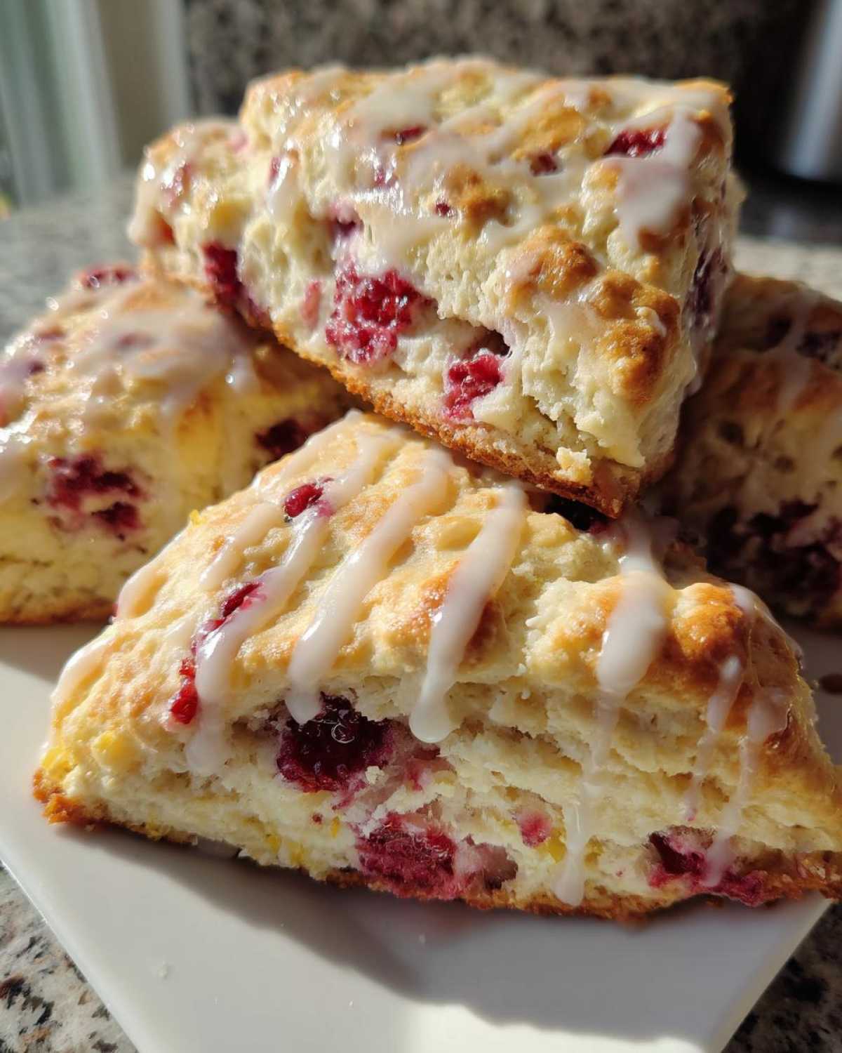 A close-up stack of freshly baked White Chocolate Raspberry Scones drizzled with a sweet white glaze.