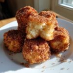 A stack of golden Air Fryer Crispy Cinnamon Sugar Biscuit Bites coated heavily in cinnamon sugar, one piece broken open.