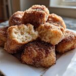 A stack of Air Fryer Crispy Cinnamon Sugar Biscuit Bites coated heavily in cinnamon sugar, with one broken open.
