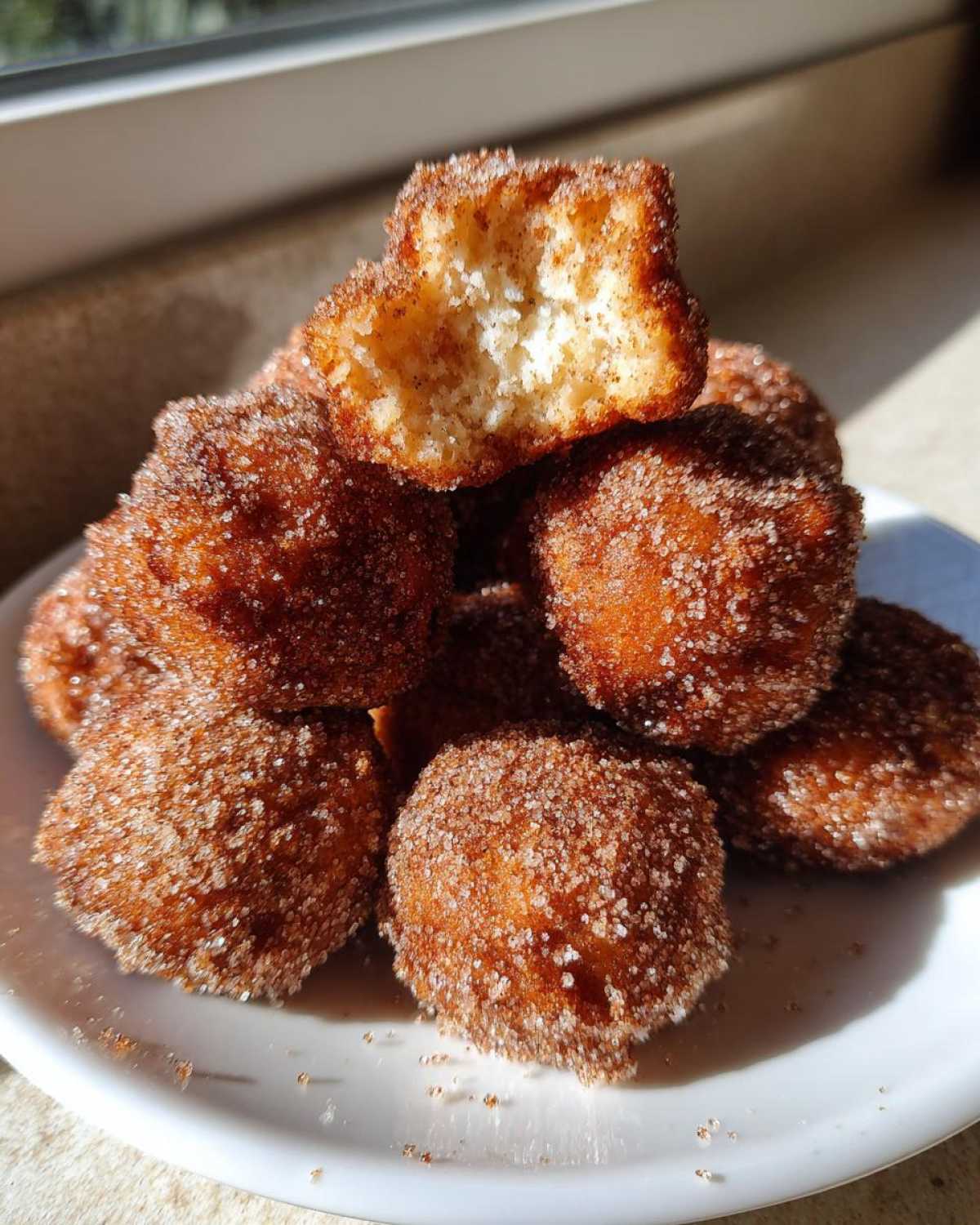 A stack of golden brown Air Fryer Crispy Cinnamon Sugar Biscuit Bites heavily coated in cinnamon sugar, one is broken open.