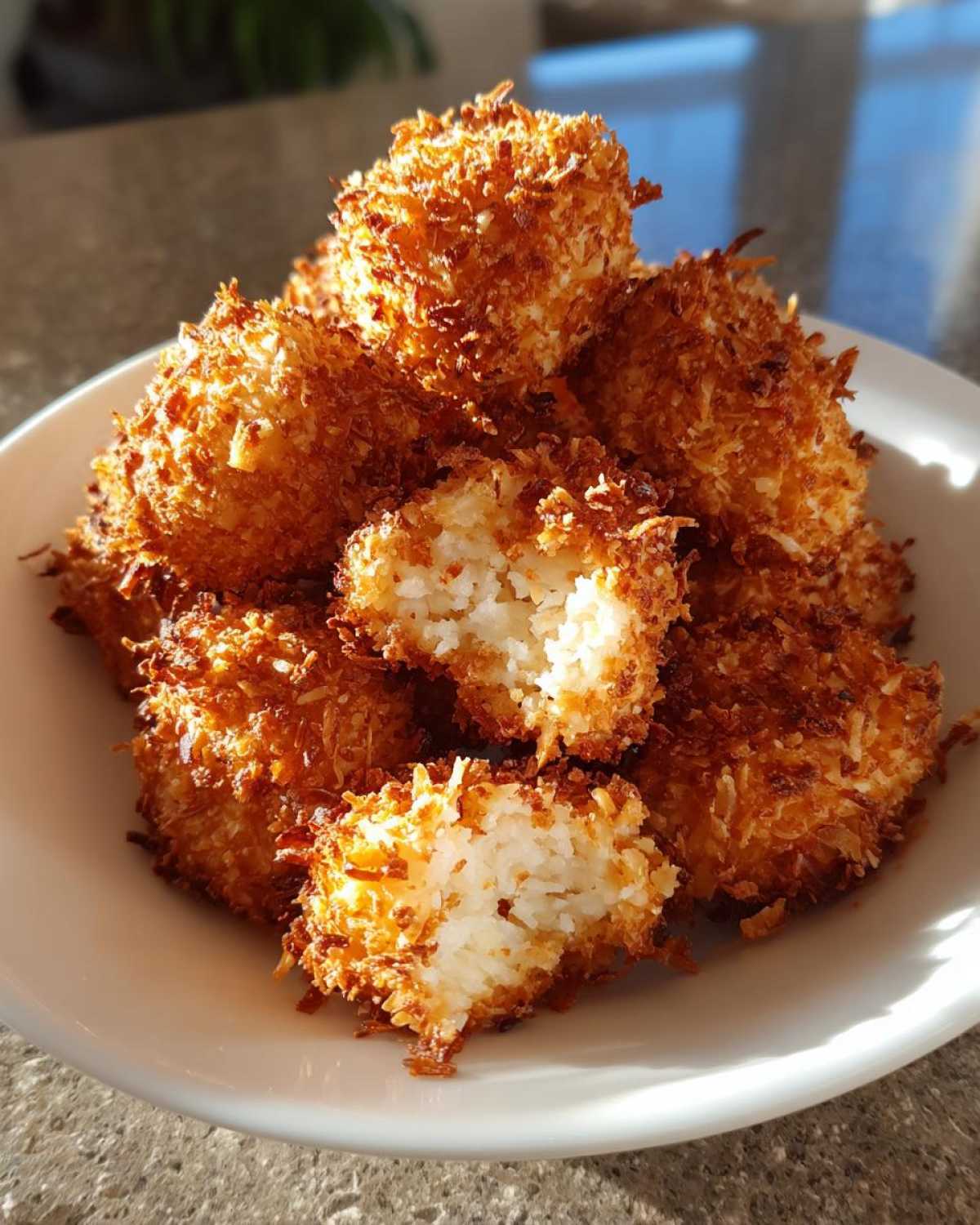 A pile of golden brown Air Fryer Crispy Coconut Chicken Bites, one is broken open showing the white interior.