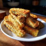 A pile of golden brown, crispy Air Fryer Crispy Garlic Dill Pickles sticks served on a white plate.