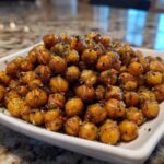 A close-up of golden brown Air Fryer Crispy Garlic Herb Chickpeas seasoned with herbs, piled high in a white square bowl.
