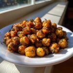 A close-up of golden, crispy Air Fryer Crispy Garlic Herb Chickpeas seasoned with herbs, piled on a white plate near a sunny window.