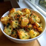 A white bowl filled with golden brown Air Fryer Crispy Garlic Parmesan Potato Cubes, garnished with fresh parsley.