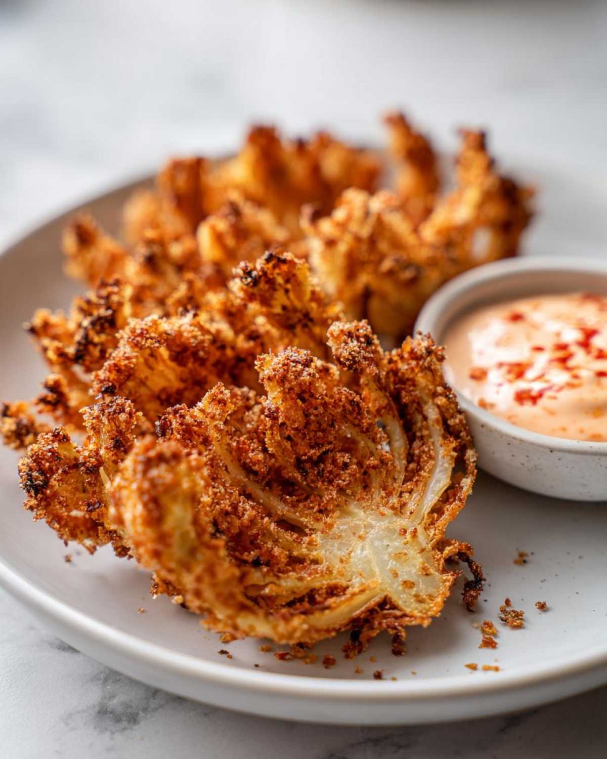 Close-up of golden brown Air Fryer Crispy Onion Petals served with a side of spicy mayo dipping sauce.