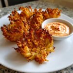 Four golden brown Air Fryer Crispy Onion Petals served on a white plate next to a small bowl of spicy mayo dip.