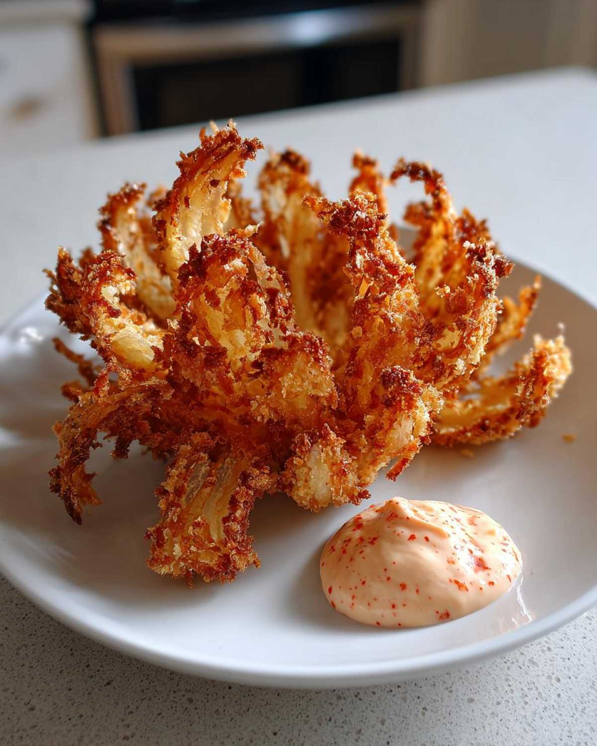 A perfectly cooked Air Fryer Crispy Onion Petals served on a white plate next to a dollop of spicy mayo.