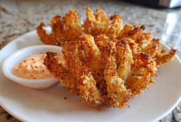 Two golden brown Air Fryer Crispy Onion Petals served on a white plate next to a small bowl of spicy mayo dipping sauce.