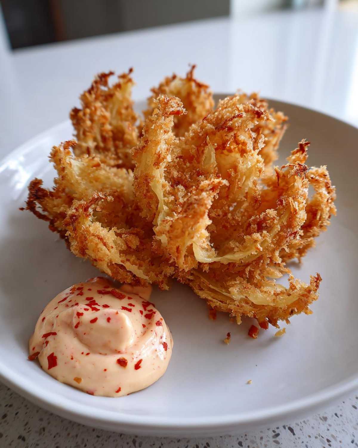 A golden brown, crispy Air Fryer Crispy Onion Petals served next to a dollop of spicy mayo dipping sauce.