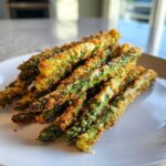 A pile of golden brown Air Fryer Crispy Parmesan Asparagus Fries stacked on a white plate.