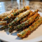 A pile of golden brown Air Fryer Crispy Parmesan Asparagus Fries served on a white plate.