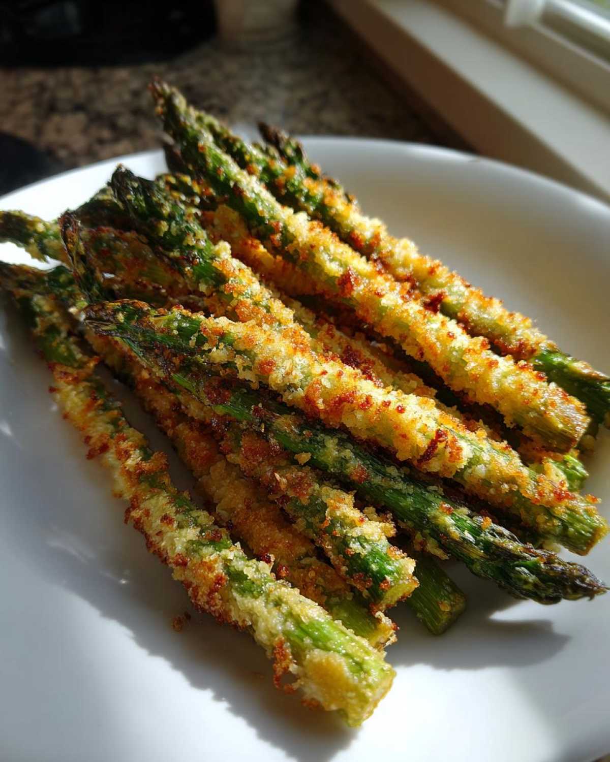 Close-up of golden brown Air Fryer Crispy Parmesan Asparagus Fries piled on a white plate.