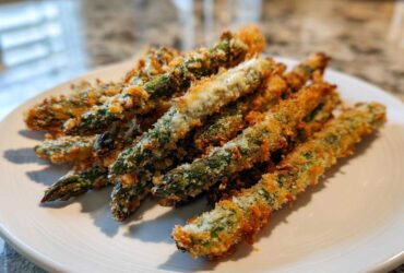 A pile of golden brown Air Fryer Crispy Parmesan Asparagus Fries served on a white plate.