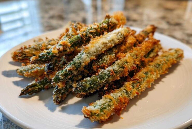 A pile of golden brown Air Fryer Crispy Parmesan Asparagus Fries served on a white plate.