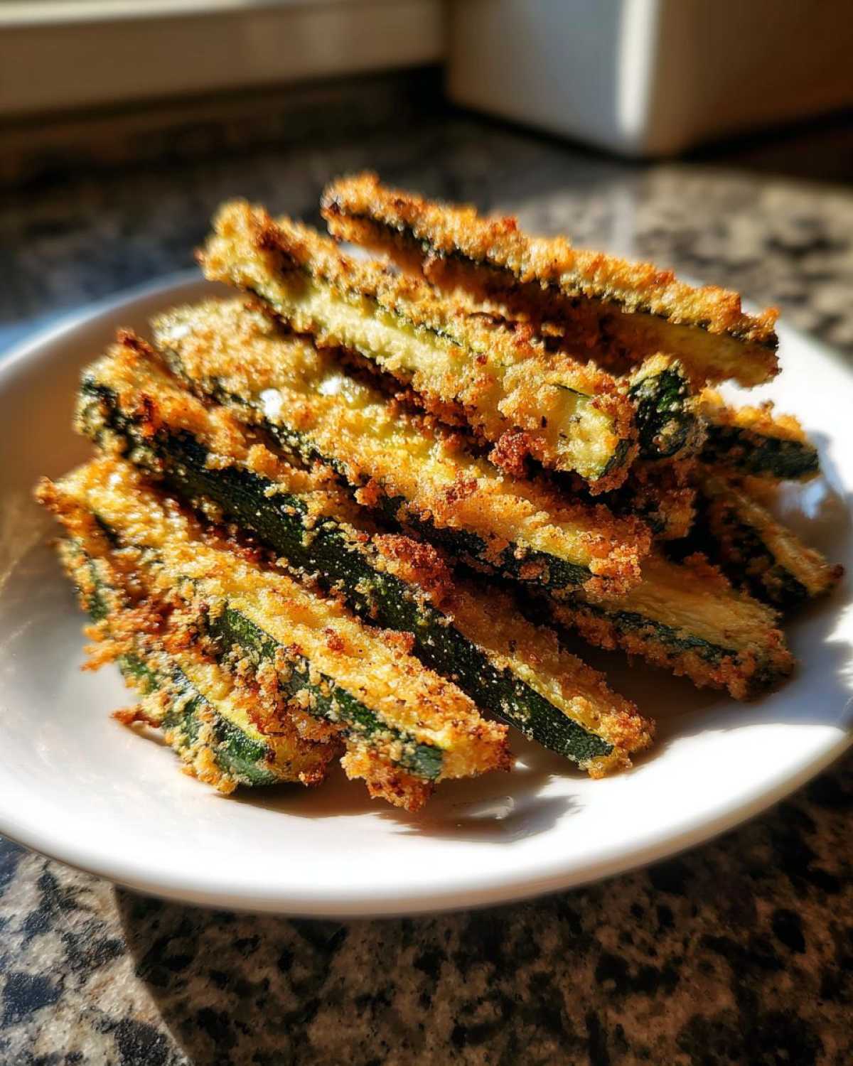 A stack of golden brown Air Fryer Crispy Parmesan Crusted Zucchini Spears piled high on a white plate.