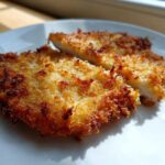 Close-up of two pieces of golden brown Air Fryer Crispy Parmesan Pork Schnitzel on a white plate.