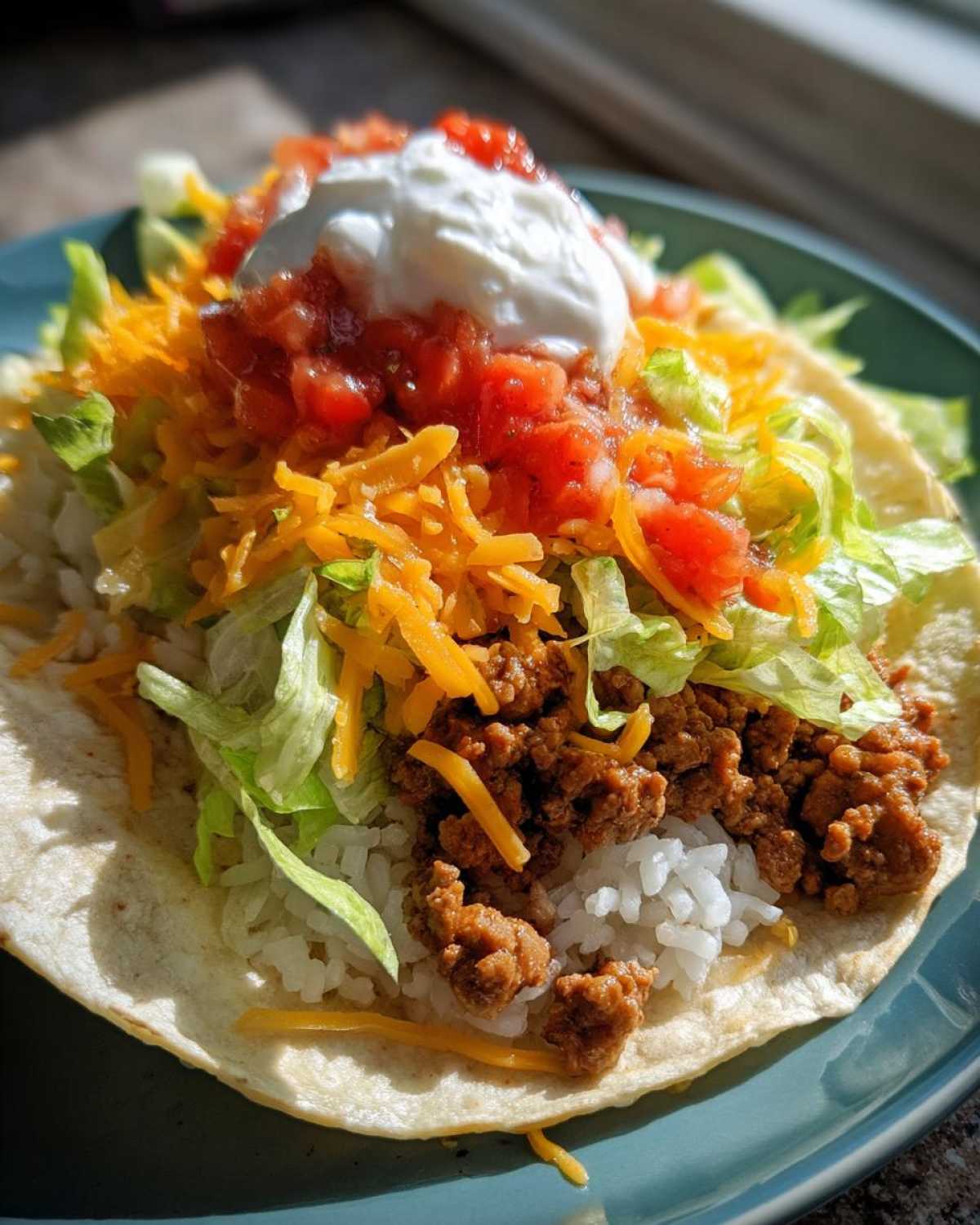 A fully loaded Air Fryer Crispy Turkey Taco Bowl served on a soft tortilla with rice, seasoned turkey, lettuce, cheese, salsa, and sour cream.