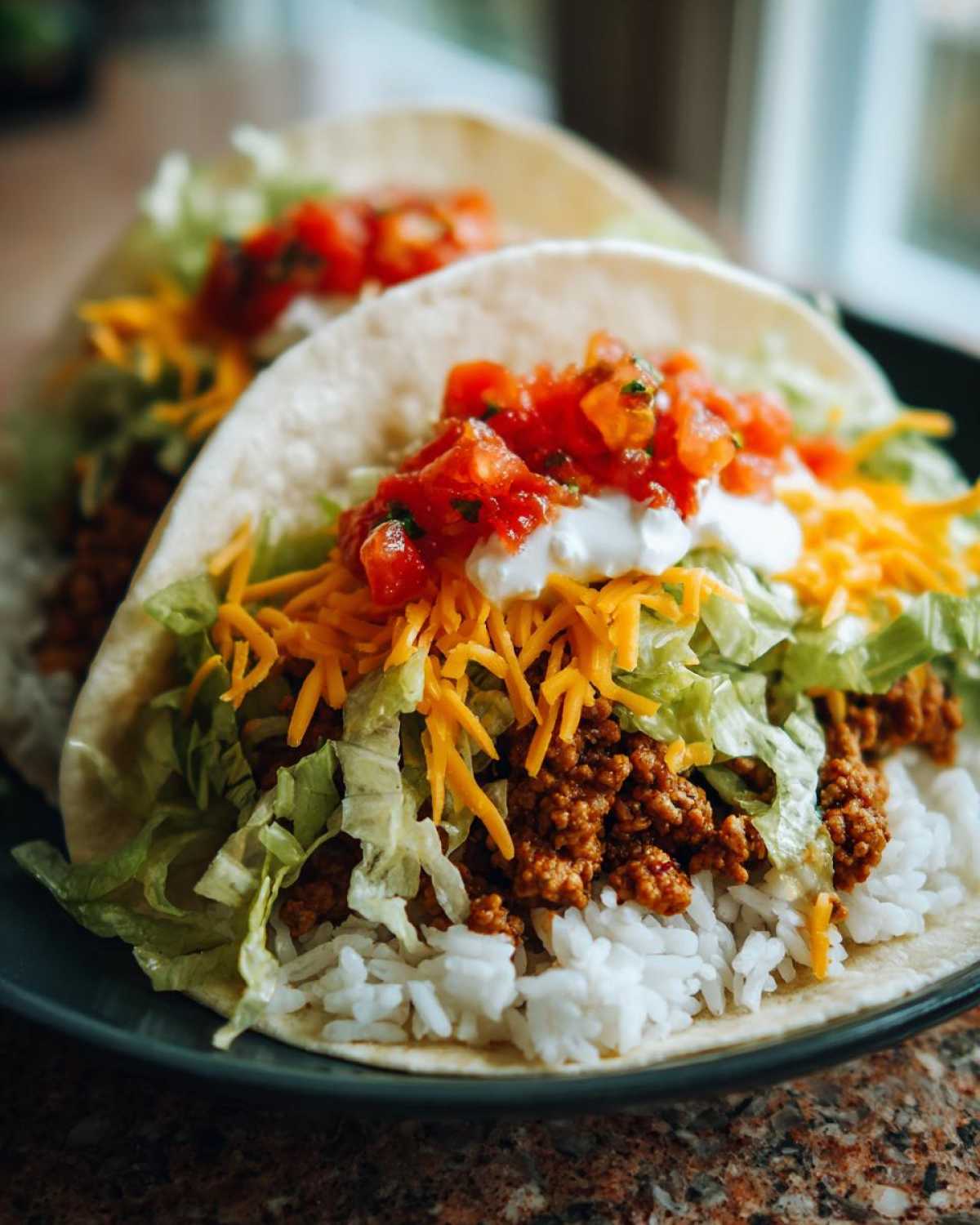 Close-up of two soft shell tacos filled with rice, seasoned ground turkey, lettuce, cheese, salsa, and sour cream, inspired by Air Fryer Crispy Turkey Taco Bowls.