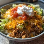 A close-up of a finished Air Fryer Crispy Turkey Taco Bowl topped with cheese, salsa, and sour cream.