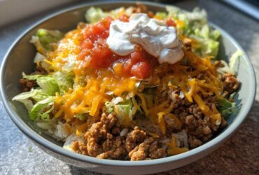A close-up of a finished Air Fryer Crispy Turkey Taco Bowl topped with cheese, salsa, and sour cream.