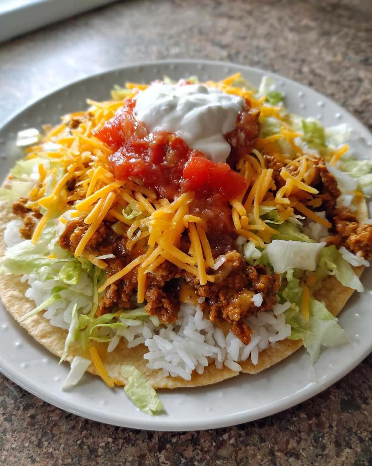 A fully loaded Air Fryer Crispy Turkey Taco Bowl served on a crispy tortilla base with rice, meat, lettuce, cheese, salsa, and sour cream.