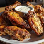 A plate piled high with golden brown, crispy Air Fryer Crispy Zaatar Chicken Wings next to a small bowl of dipping sauce.