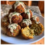 A pile of crispy Air Fryer Herb Falafel Balls drizzled with creamy tahini sauce and sprinkled with parsley.