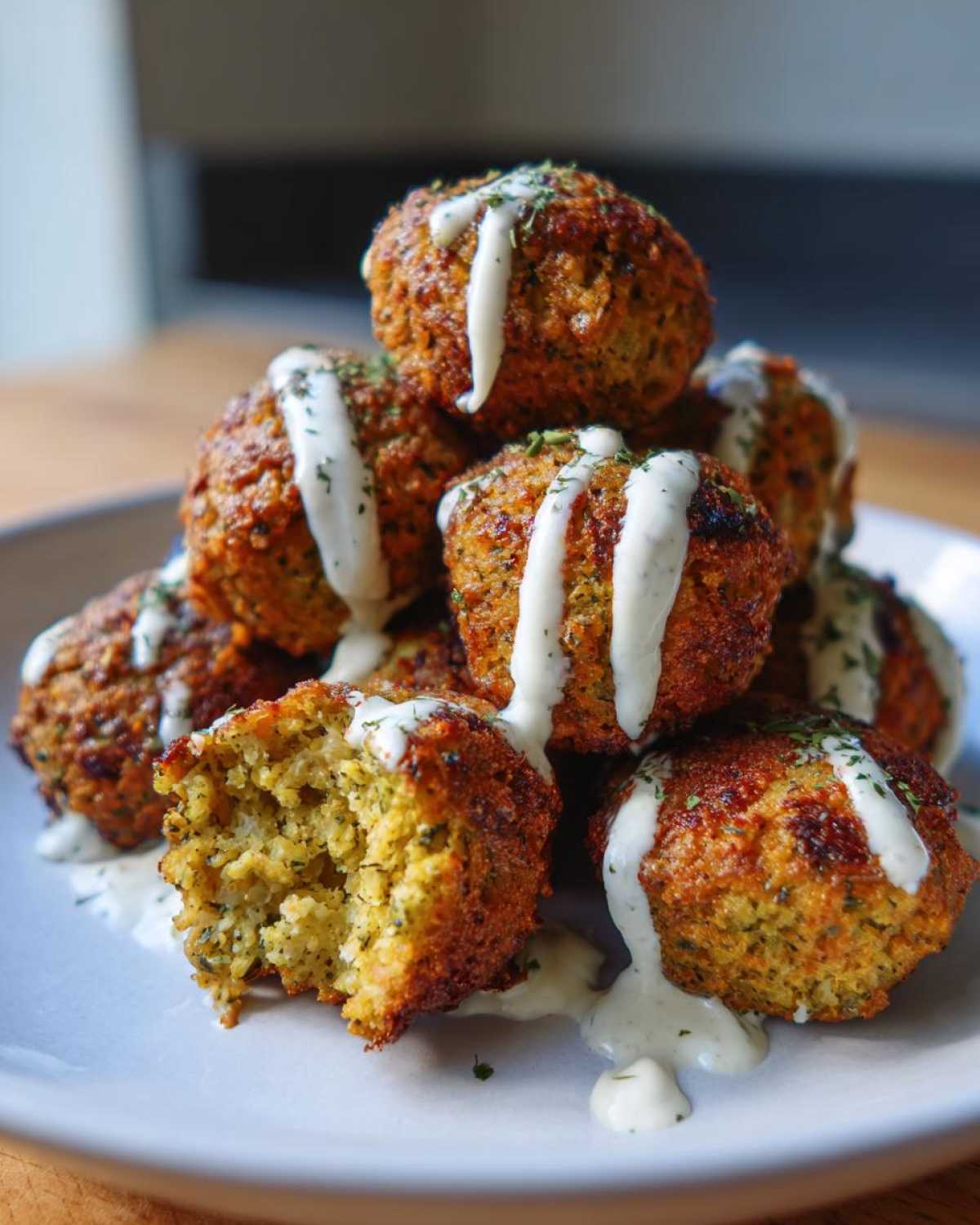 A stack of golden brown Air Fryer Herb Falafel Balls drizzled with white tahini sauce and sprinkled with herbs