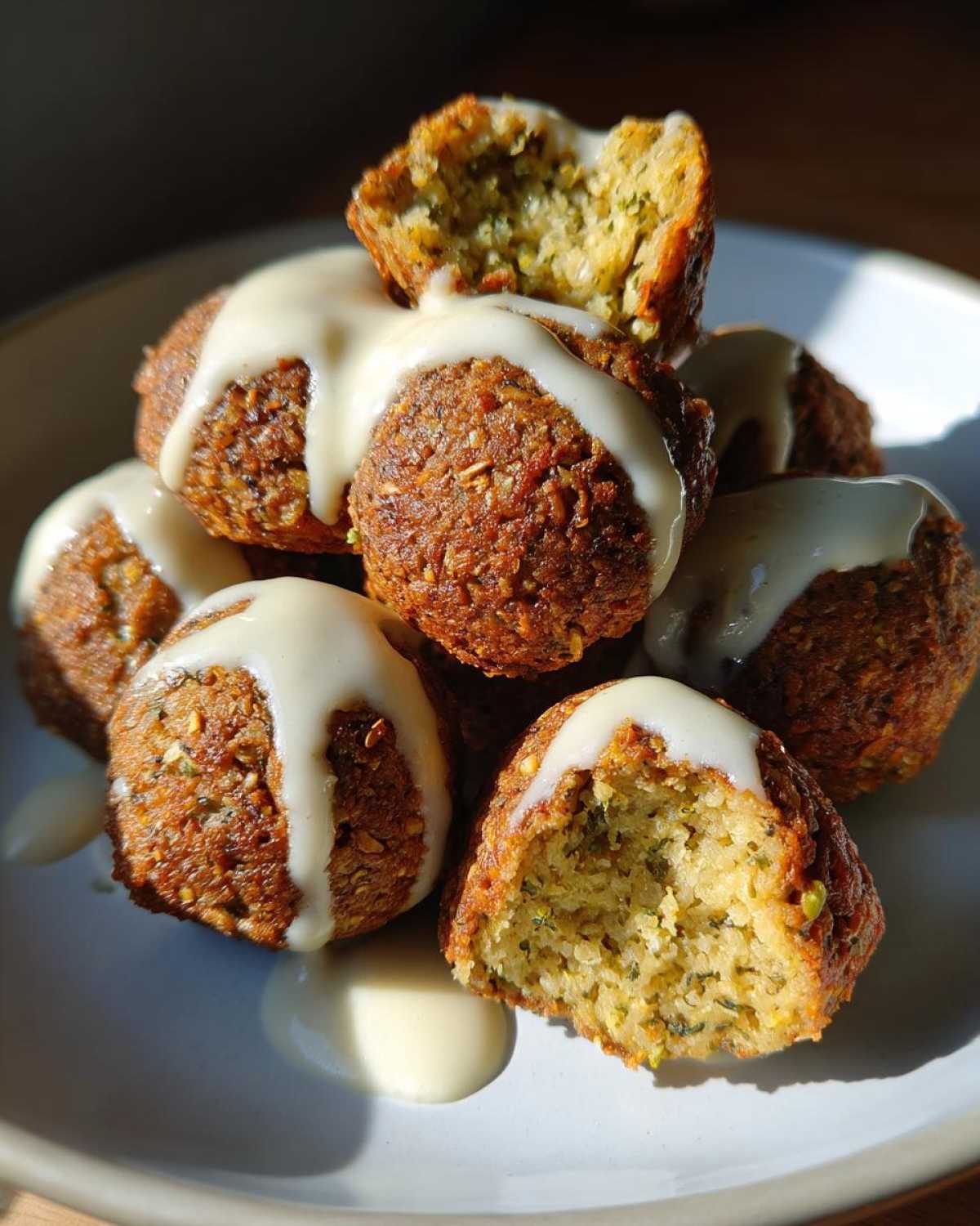 A stack of golden brown Air Fryer Herb Falafel Balls drizzled generously with creamy white tahini sauce.
