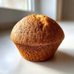 Close-up of a golden brown, domed Apple Cinnamon Muffin showing specks of cinnamon on the crust.