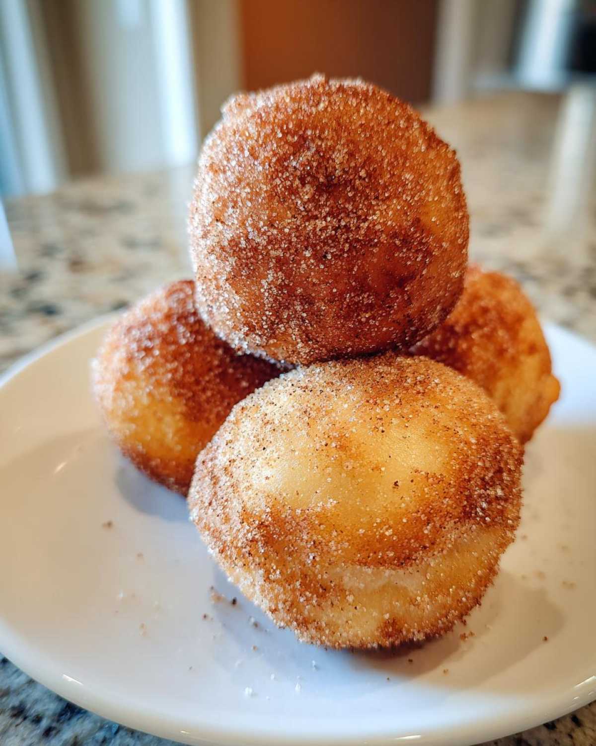Four golden-brown Apple Pie Bombs coated generously in cinnamon sugar, stacked on a white plate.