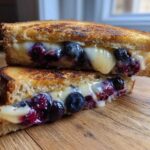 Two halves of a perfectly grilled Blueberry Grilled Cheese stacked, showing melted cheese and bursting blueberries.