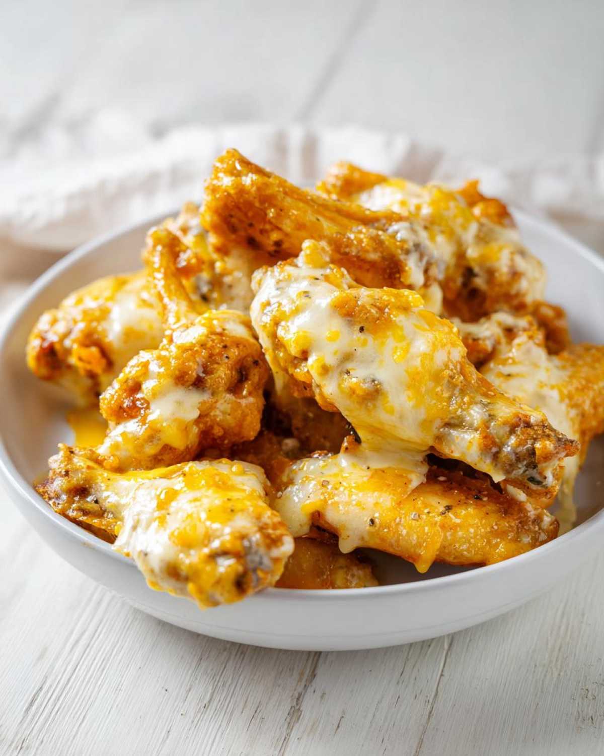 Close-up of crispy chicken wings generously coated in melted cheese and Copycat Garlic Parmesan Wing Sauce in a white bowl.