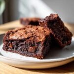 Close-up of two fudgy Chocolate Root Beer Brownies stacked on a light plate, showing melted chocolate chips.