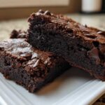 Two rich, fudgy slices of Chocolate Root Beer Brownies stacked on a white plate, topped with chocolate chips.