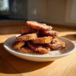 A tempting pile of golden Cinnamon Sugar Banana Chips heavily coated in sparkling sugar and spice, served on a small white plate.