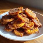 A close-up shot of a generous pile of golden Cinnamon Sugar Banana Chips stacked on a white plate.