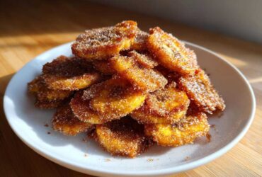 A close-up shot of a generous pile of golden Cinnamon Sugar Banana Chips stacked on a white plate.