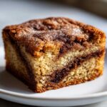 A close-up, appetizing shot of a square Cinnamon Swirl Snickerdoodle Blondies slice with a visible cinnamon swirl and sugary topping.