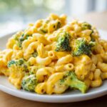 A close-up of creamy Copycat Café Broccoli Cheddar Mac with elbow macaroni and bright green broccoli florets.