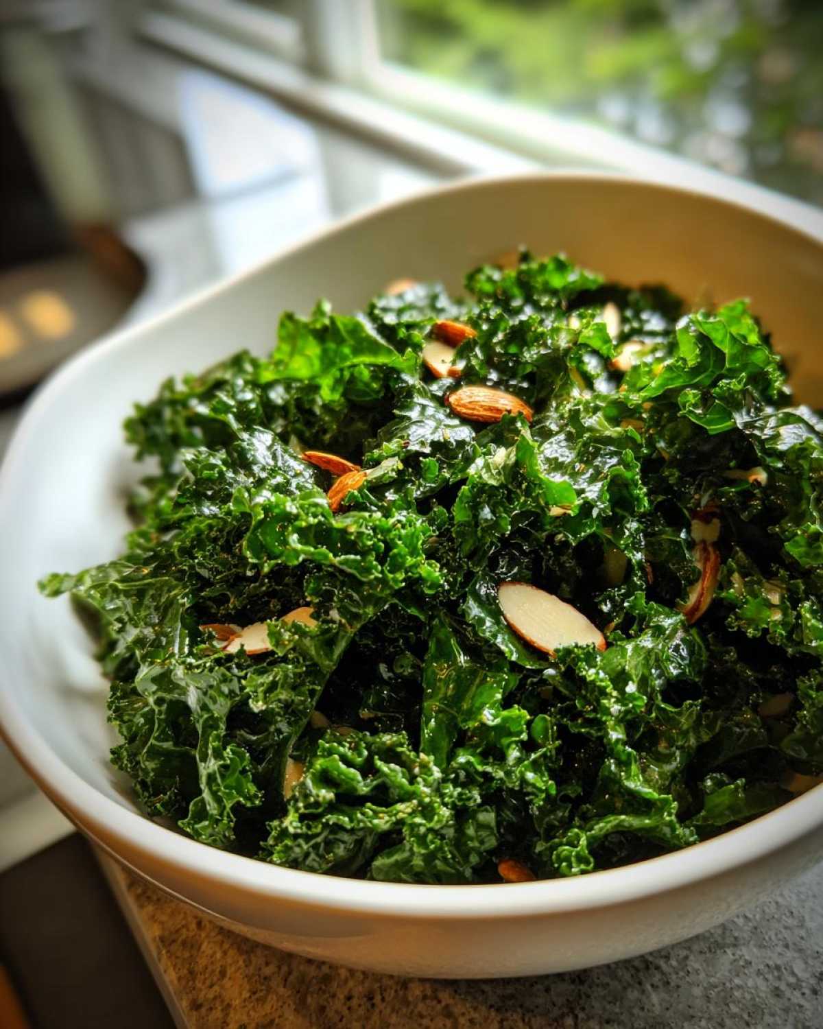 A close-up shot of massaged kale tossed with sliced almonds, ready to serve as Copycat Kale Crunch Salad.