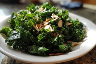 A vibrant close-up of Copycat Kale Crunch Salad tossed with dressing and topped with toasted sliced almonds on a white plate.