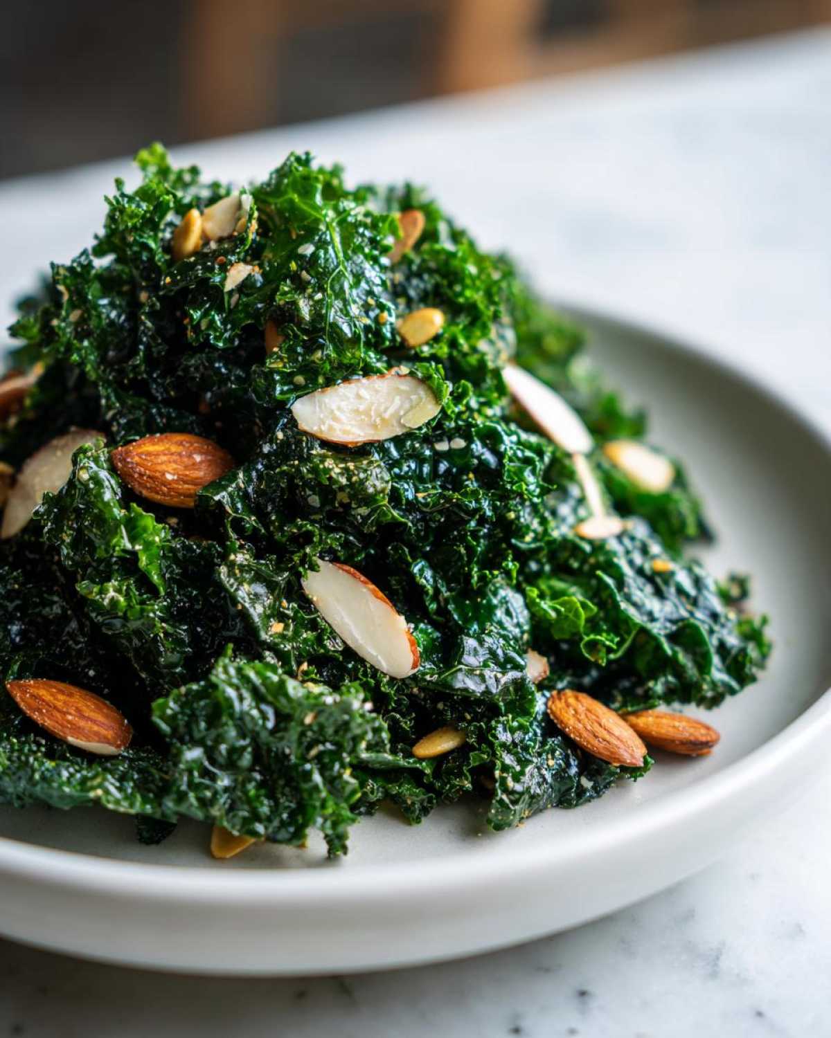 A close-up of a mound of massaged kale, part of the Copycat Kale Crunch Salad, topped with sliced almonds and seeds.