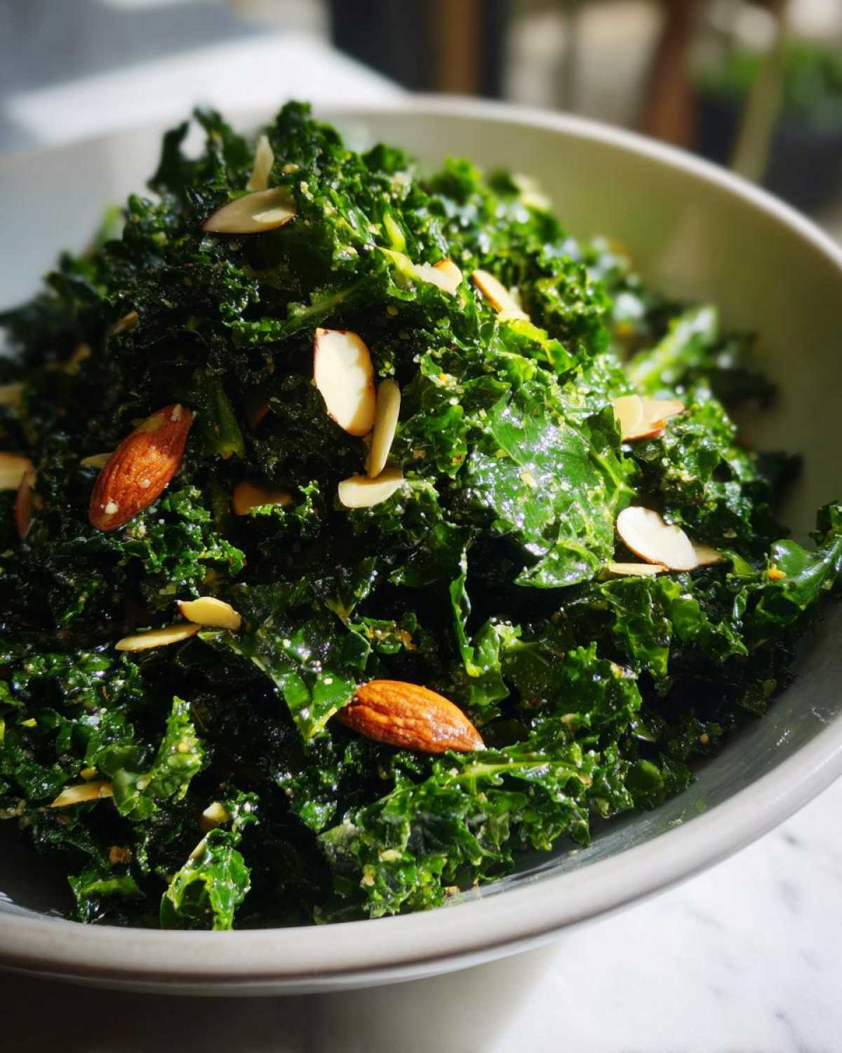 A close-up view of a bowl filled with massaged kale, topped with sliced and whole almonds, representing the Copycat Kale Crunch Salad.