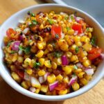 Close-up of charred corn kernels mixed with diced red onion, tomato, and cilantro in a white bowl, showcasing the Copycat Mexican Grill Corn Salsa.